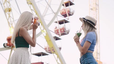 Two friends enjoy a fun day at the carnival, taking photos while sipping Stock Footage 312779641