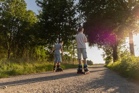 Two friends enjoy inline skating on a gravel path surrounded by trees and g.. Stock Photos