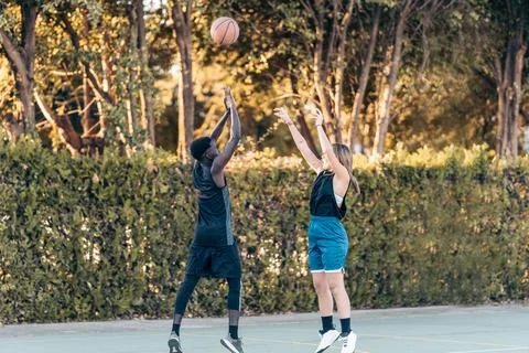 Two friends fighting for a ball while jumping in a basketball match Stock Photos