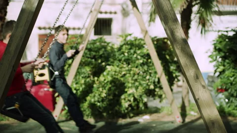 Two friends happily swing from a swing set outside on a playground and having fu Stock Footage 199457066