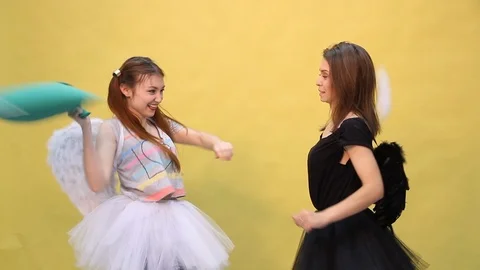 Two friends have fun fighting pillows in the form of an angel and a demon Stock Footage 103186651
