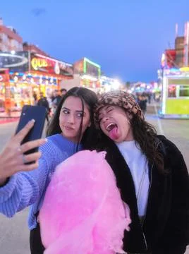 Two friends joking while taking selfie holding a cotton candy in a night fair Stock Photos