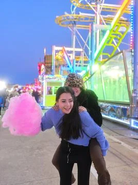 Two friends jumping on the back and joking while holding a cotton candy outdoors Stock Photos