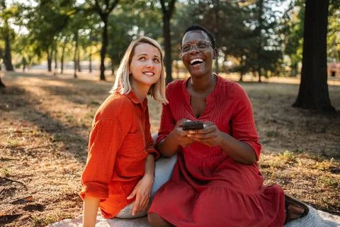 Two friends laughing while looking up in a park during sunset Stock Photos