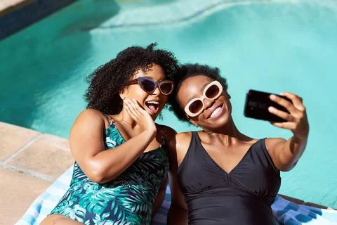 Two friends lying by the pool taking selfies in swimsuits, body positive summer Stock Photos