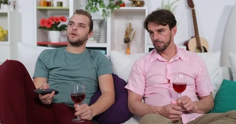Two Friends Men Zapping the Remote Control Holding Cup of Red Wine Sit on Couch Stock Footage 88027886