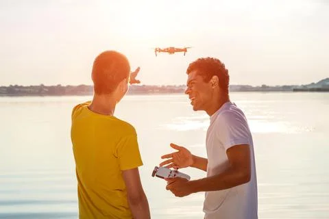 Two friends operating drone with controller standing near the river Stock-Fotos