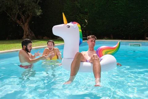 Two friends planning throwing man from a rainbow unicorn float into the pool. Stock Photos