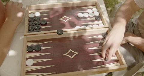 Two friends playing a game of backgammon outside on a sunny day, enjoying Stock Footage 280565728