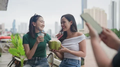 Two friends posing for a photo while holding a coconut drink and a cold beverage Stock Footage 319761608