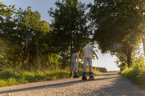 Two friends practice inline skating on a dirt path surrounded by trees. It'.. Stock Photos