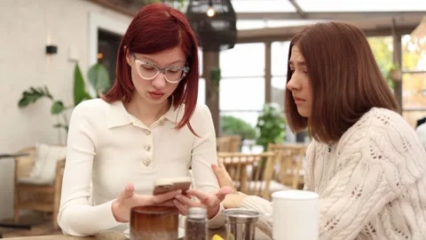 Two friends sit in a cozy cafe one reading upsetting news  Video stock 320827261