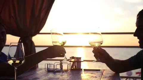 Two friends sit by the sea at sunset with glasses of wine in hands. HD Video stock 79782056