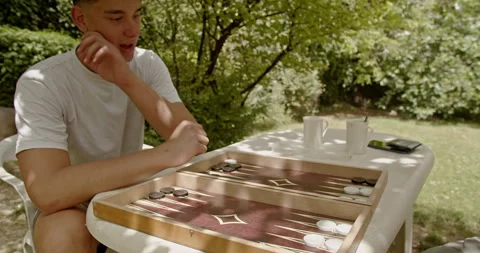 Two friends sit at a table outside, deeply focused on a game of backgammon Stock Footage 281966411