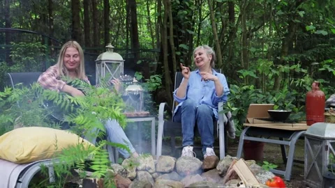Two friends sitting around a fire in the summer, roasting vegetables, chatting a Vídeos de archivo 277568490