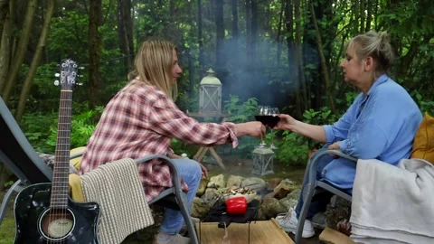 Two friends sitting around a fire in the summer, roasting vegetables, chatting a Vídeos de archivo 277568495