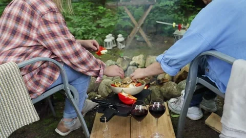 Two friends sitting around a fire in the summer, roasting vegetables, chatting a Stock Footage 277568497