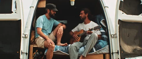 Two friends sitting in back of a van having fun and playing the guitar Stock Footage 203584455