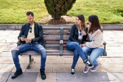 Two friends sitting on a bench next to an unknown boy. 스톡 사진