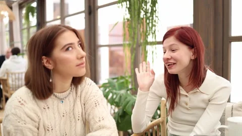 Two friends sitting in a cafe chatting one girl excitedly talks about her new bo Stock Footage 320827348