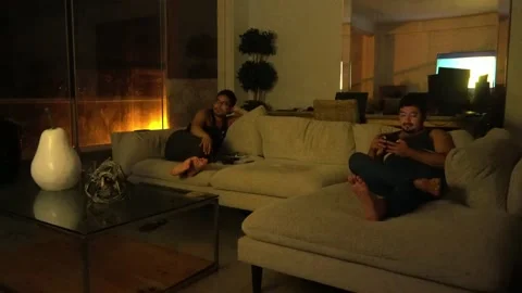 Two friends sitting on the couch watching a movie on tv in the living room of a Video stock 186216653