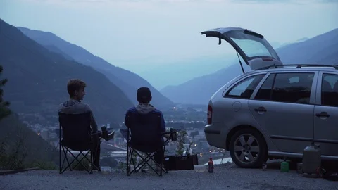 Two friends sitting in deck chairs besides car, toasting with a beer, 4K Stock Footage 129613833