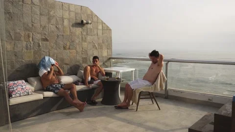 Two friends sitting talking and drinking beer on the terrace of the beach house Stock Footage 189112052