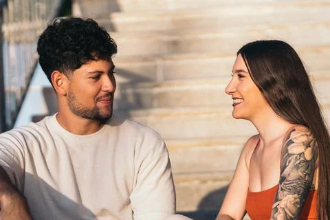 Two friends smiling while talking on an outdoor stairs during sunset Stock Photos