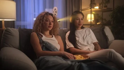 Two friends spend time watching movies on a projector. The young women are Stock Footage 263984273
