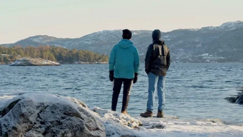 Two friends standing towards the sunset on a winter island. looking out to sea Stock Footage 233898285