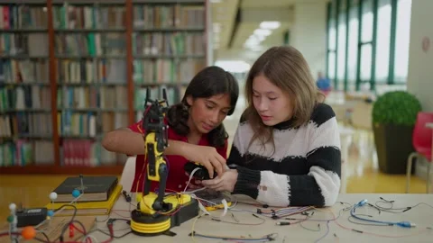 Two friends studying a robotic arm while using a remote controller in library 動画素材 326640732