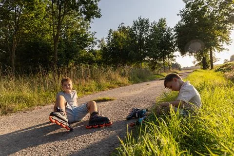 Two friends take a break while inline skating on a quiet path. The sun shin.. Stock Photos