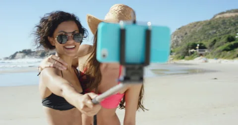 Two friends taking selfies on the beach using selfie stick Stock Footage
