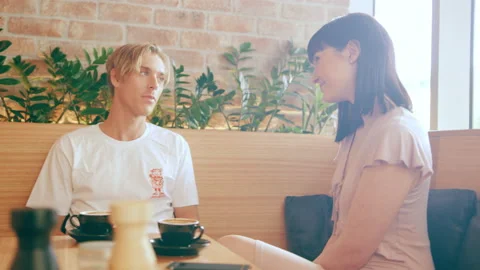 Two friends talking and drinking coffee at a booth in interior cafe with soft da Stock Footage 199455423