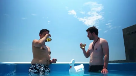 Two friends talking and toasting with whiskey in glass glasses inside a pool on Video stock 173506368