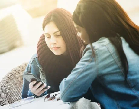 Two friends talking and using the mobile phone. Stock Photos
