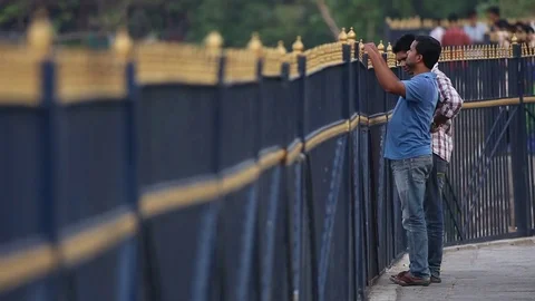 Two friends talking near tall fence on sidewalk India Stock Footage 73348070