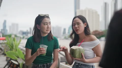 Two friends talking outdoors while holding a coconut drink and a cold beverage Stock Footage 319762393