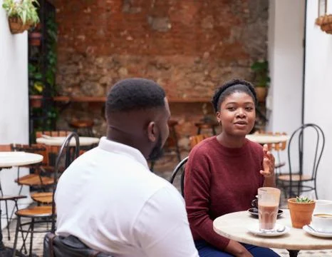Two friends talking over drinks in a trendy cafe courtyard Foto stock