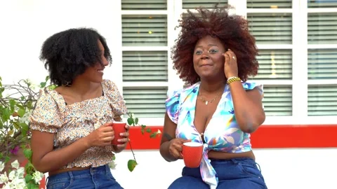 Two friends talking together as they sit outside the house drinking coffee Видео 235397794