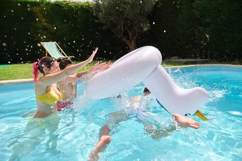 Two friends throwing man from a rainbow unicorn float into the pool. Stock Photos