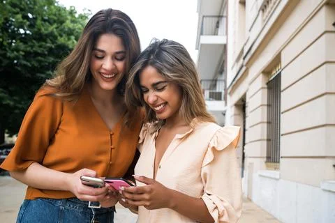 Two friends using mobile phone outdoors. Stock Photos