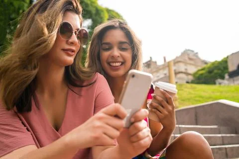 Two friends using mobile phone outdoors. Stock Photos