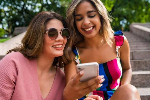 Two friends using mobile phone outdoors. Stock Photos