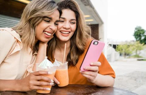 Two friends using phone at coffee shop outdoors. Stock Photos