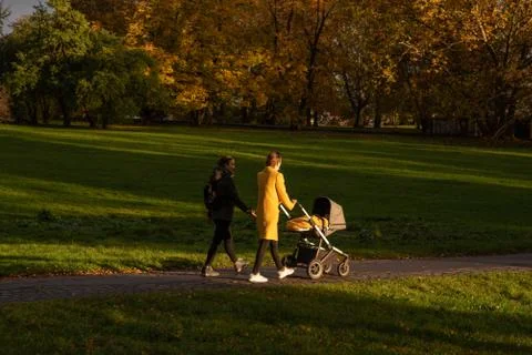 Two friends walking on the park while one is carrying a stroller with a baby Stock Photos