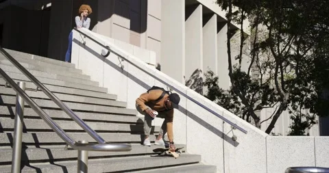 Two friends watching man retrieving skateboard after slipping, sitting eating Stock Footage 340068877