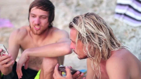 Two friends watching media content in a smart phone sitting on the beach Stock-Footage 82147397