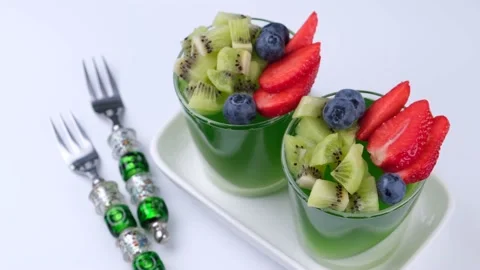 Two fruit jelly green desserts in glasses with kiwi strawberries and blueberries Stock Footage 196967595