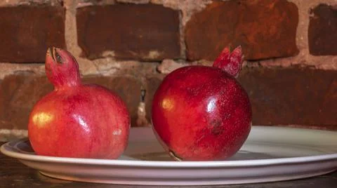 Two fruit juicy Spanish pomegranate on porcelain plate on a red brick wall ba 스톡 사진